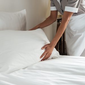 Cropped image of a female chambermaid making bed in hotel room